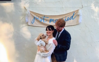 a married couple holding a dog and standing in front of a just married sign hanging on the wall behind them
