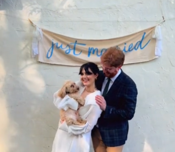 a married couple holding a dog and standing in front of a just married sign hanging on the wall behind them